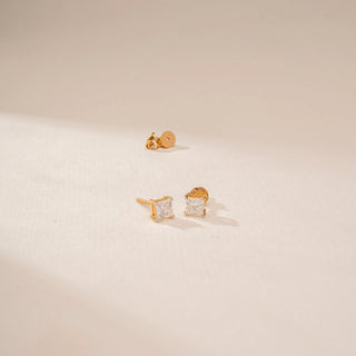 Angled view of 14KT Yellow Gold diamond stud earrings, featuring square-cut diamonds in four-prong settings.