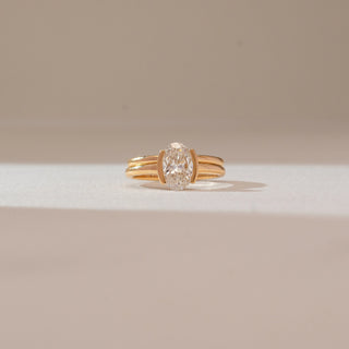 Front view of oval diamond ring in yellow gold, featuring a central lab-grown diamond held between parallel band accents. Captured against a soft beige background with gentle shadows.