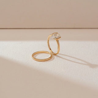 Side angled view of solitaire diamond ring set in yellow gold, featuring a round lab-grown diamond alongside a matching plain gold band. Captured against a soft beige textured background.