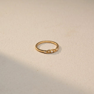 Top view of a diamond accent ring in 14 KT Yellow Gold, featuring three round lab-grown diamonds nestled between geometric gold motifs on a slim band, displayed against a beige backdrop.