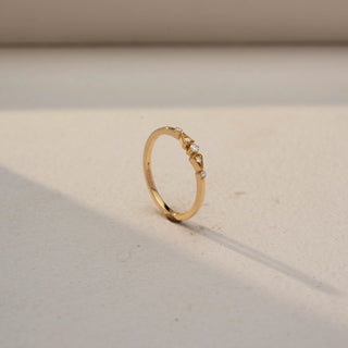 Angled view of a diamond accent ring in 14 KT Yellow Gold, featuring three round lab-grown diamonds nestled between geometric gold motifs on a slim band, displayed against a beige backdrop.