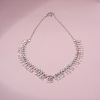 Top view of a floral lab-grown diamond necklace in 14KT White Gold, featuring cascading marquise and pear-shaped diamond motifs in a fringe design. Captured against a pink backdrop, the elegant silhouette radiates brilliance.