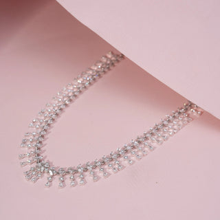Angled view of a floral lab-grown diamond necklace in 14KT White Gold, featuring cascading pear-shaped diamond motifs in a graceful fringe design. Captured against a pink backdrop, the elegant silhouette radiates brilliance.