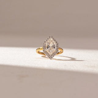 Front view of Hexagon Halo Diamond Ring in 14KT Yellow Gold, featuring a large center diamond encircled by a pavé halo. Set on a soft beige surface, the design reflects refined brilliance and symmetry.
