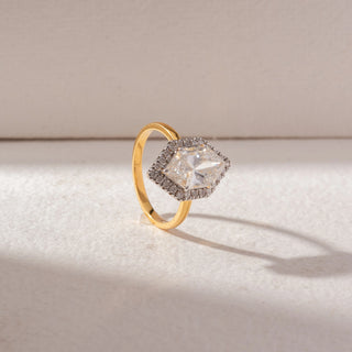 Angled view of Hexagon Halo Diamond Ring in 14KT Yellow Gold, featuring a large center diamond encircled by a pavé halo. Set on a soft beige surface, the design reflects refined brilliance and structure.
