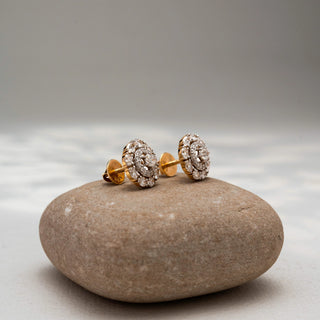 Side view of round diamond stud earrings in 14 KT Yellow Gold, featuring concentric halo circles with brilliant center diamonds, displayed on a textured stone surface.
