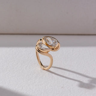 Side view of Toi Et Moi Diamond Ring in 14KT Yellow Gold, featuring pear-shaped and oval lab grown diamonds in fluid wrap settings. Set on a beige backdrop, the design highlights structure and modern elegance.
