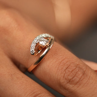 A top view of a 14 KT rose gold ring, modelled on a hand of size 13.5, featuring an asymmetrical twist design with one side of the band having lab-grown round cut diamonds in prong setting with a total of 0.429 carat that curve into a loop and weighing 3.61 grams making it simple and unique for any occasion and everyday wear.