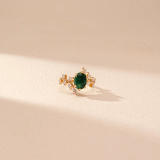 Top view of a 14KT yellow gold ring featuring a green emerald with round and marquise-cut diamonds, set against a beige background.