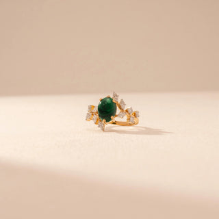 Side view of a 14KT yellow gold ring featuring a green emerald with round and marquise-cut diamonds, set against a beige background.