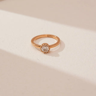 Top view of Reia’s 14 KT Rose Gold Classic Bezel Diamond Solitaire Ring. It features a brilliant round diamond in a modern bezel setting on a warm gold band against a soft neutral backdrop.