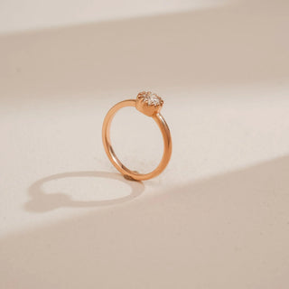 Side view of Reia’s 14 KT Rose Gold Classic Bezel Diamond Solitaire Ring. It features a round brilliant diamond in a sleek bezel setting on a polished gold band against a neutral backdrop.