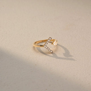 Side view of a geometric open ring in 14 KT Yellow Gold, featuring a vertical bar of round lab-grown diamonds paired with a bezel-set trillion-cut diamond in a modern open design, displayed against a beige backdrop.