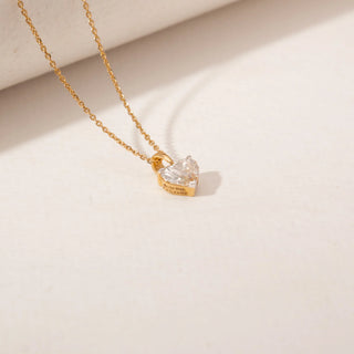 Top view of a heart-shaped diamond pendant in 14KT Yellow Gold, featuring a solitaire stone on a delicate chain against a beige backdrop.