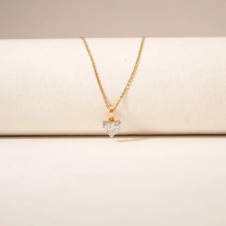 Close-up view of a heart-shaped diamond pendant in 14KT Yellow Gold, featuring a solitaire stone on a delicate chain against a beige backdrop.