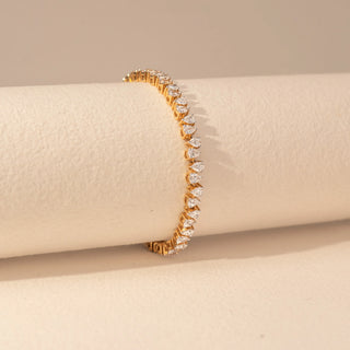 Side view of a 14KT yellow gold bracelet featuring pear-cut diamonds, set against a beige background.