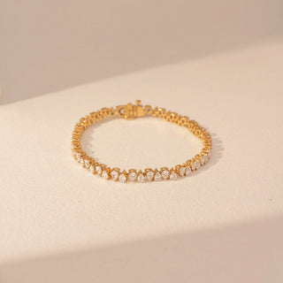 Top view of a 14KT yellow gold bracelet featuring pear-cut diamonds, set against a beige background.