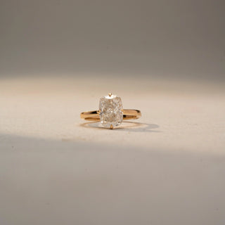 Front view of a cushion-cut solitaire ring in 14 KT Yellow Gold, featuring a cushion-cut lab-grown diamond in a classic four-prong setting, displayed against a beige backdrop.