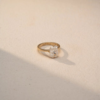 Side view of a cushion-cut solitaire ring in 14 KT Yellow Gold, featuring a cushion-cut lab-grown diamond in a classic four-prong setting, displayed against a beige backdrop.
