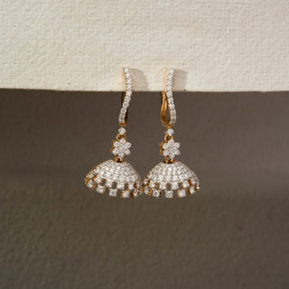 Front view of floral diamond jhumka earrings in 14 KT Yellow Gold, featuring pavé-set domes, flower motifs, and cascading diamond accents against a neutral textured backdrop.

