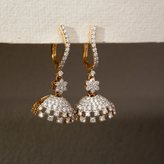 Close view of floral diamond jhumka earrings in 14 KT Yellow Gold, featuring curved pavé hoops, flower motifs, and shimmering dome drops against a neutral backdrop.
