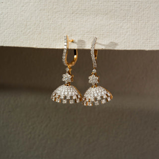 Side view of floral diamond jhumka earrings in 14 KT Yellow Gold, featuring curved pavé hoops, flower motifs, and shimmering dome drops against a neutral textured backdrop.
