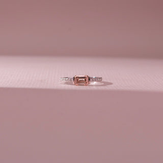 Front view of emerald-cut pink gemstone ring with a pavé diamond band in white gold, set on a soft pink textured surface, highlighting delicate color and clean, geometric sparkle.