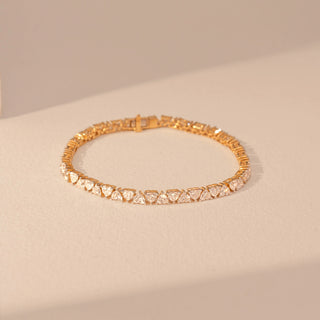 Top view of a 14KT yellow gold bracelet featuring heart-cut diamonds, set against a beige background.