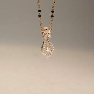Side view of a diamond mangalsutra pendant in 14KT Yellow Gold, featuring an open teardrop design with a dangling pear-cut diamond. Captured against a beige backdrop, it exudes graceful sparkle.