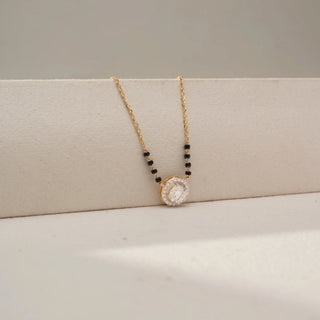 Side view of a diamond halo mangalsutra necklace in 14 KT Dual Gold, featuring an oval-cut lab-grown diamond encircled by a sparkling halo, accented with black beads and displayed on a beige backdrop.