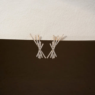 Front view of diamond statement earrings in 14 KT Yellow Gold, featuring intersecting pavé-set bars arranged in an abstract burst design against a neutral textured backdrop.
