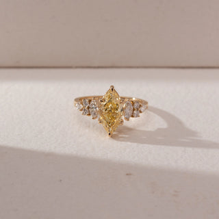 Top view of a yellow gold ring featuring a marquise-cut yellow lab-grown diamond centre stone, accented by marquise and round side diamonds. Captured against a beige backdrop, the clustered design highlights brilliance and symmetry.