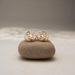 Front view of abstract diamond stud earrings in 14 KT Yellow Gold, featuring layered pavé-set oval frames with clustered marquise and pear-shaped diamond accents, displayed on a textured stone surface.
