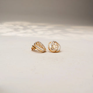 Angled view of abstract diamond stud earrings in 14 KT Yellow Gold, featuring layered pavé-set oval frames with clustered marquise and pear-shaped diamond accents, displayed on a textured stone surface.

