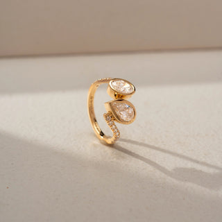 Side view of a bypass diamond ring in 14 KT Yellow Gold, featuring bezel-set pear-shaped and oval lab-grown diamonds with pavé diamond accents along the split band, displayed against a beige backdrop.