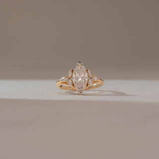 Front view of marquise diamond ring in yellow gold, featuring a central lab-grown diamond with marquise side stones along a split band. Captured against a soft beige background with subtle shadows.