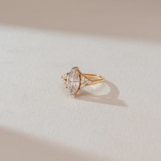 Side angled view of marquise diamond ring in yellow gold, featuring a central lab-grown diamond with marquise side stones. Captured against a soft beige textured background with gentle shadows.