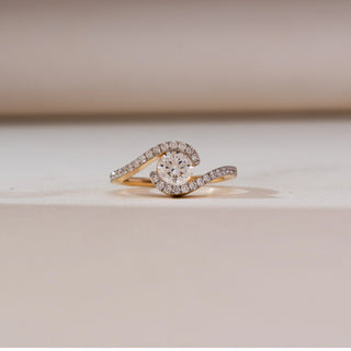 Front view of Swirling Wave Solitaire Diamond Ring in 14KT yellow gold, featuring a round centre diamond embraced by two curved pavé-set diamond bands in a wave design.