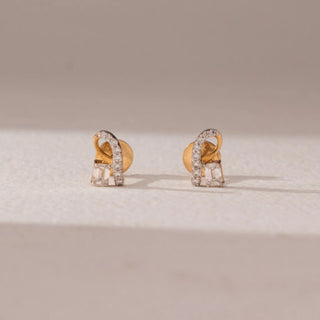 Front view of diamond stud earrings in 9KT yellow gold, featuring curved pavé diamond loops with baguette-cut diamond accents, displayed on a beige surface highlighting modern elegance and sparkle.
