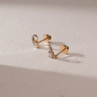 Side view of diamond stud earrings in 9KT yellow gold, featuring curved pavé loops with baguette-cut diamond accents and screw backs, set on a beige surface highlighting detail and sparkle.
