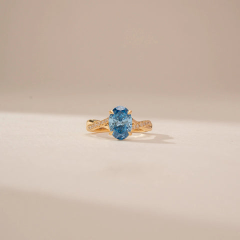 Front view of a 14KT Yellow Gold diamond ring, featuring an oval blue centre stone and diamond-set shoulders.