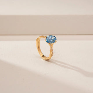 Angled view of a 14KT Yellow Gold diamond ring, featuring an oval blue centre stone and diamond-set shoulders.