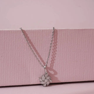 Front view of white gold pendant featuring a floral cluster of marquise-cut lab grown diamonds arranged like petals, suspended on a fine chain against a soft pink textured background.