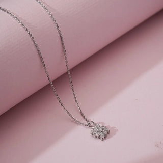 Side view of white gold diamond cluster pendant with closely set lab grown diamonds forming a floral-inspired motif, suspended on a delicate chain over a soft pink backdrop.