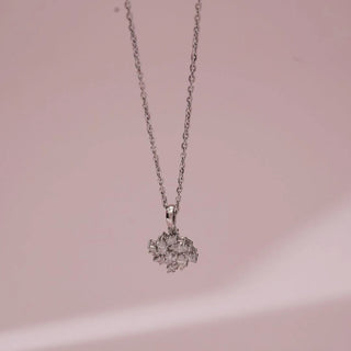Front view of white gold diamond cluster pendant featuring closely set lab grown diamonds forming a floral-inspired design, suspended on a fine chain against a soft pink background.