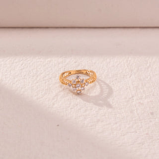 Top view of floral cluster diamond ring in yellow gold, featuring round lab-grown diamonds in a blooming cross formation. Placed on a textured beige surface, the design casts a soft, elegant shadow.