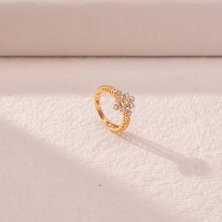 Side view of floral cluster diamond ring in yellow gold, featuring round lab-grown diamonds in a blooming cross motif. Set on a textured beige surface, the design casts a soft elongated shadow.