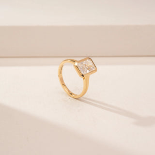 Angled view of a 14KT Yellow Gold diamond ring, featuring a rectangular step-cut centre diamond in a bezel setting.