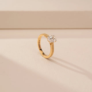 Angled view of a 14KT Yellow Gold diamond ring with an oval centre diamond and textured braided shoulders.