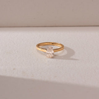 Top view of a diamond ring in 14KT yellow gold, featuring a pear-shaped center diamond in a prong setting on a sleek band, set on a beige surface highlighting refined sparkle and elegance.
